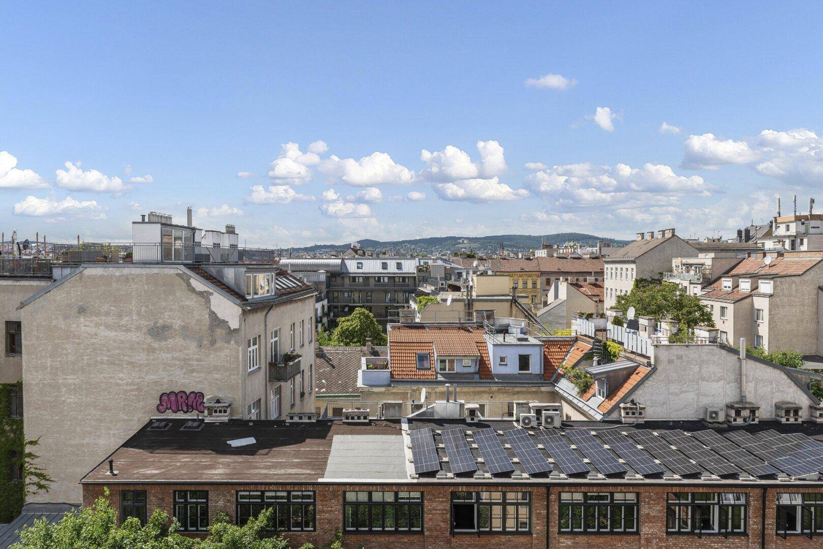 Panoramablick über die Stadt mit Dächern, Gebäuden und fernen Hügeln unter blauem Himmel.