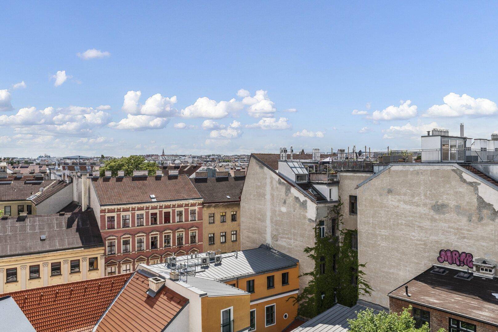 Urbane Dachlandschaft mit historischen Gebäuden und einem weiten Blick über die Stadt unter blauem Himmel.