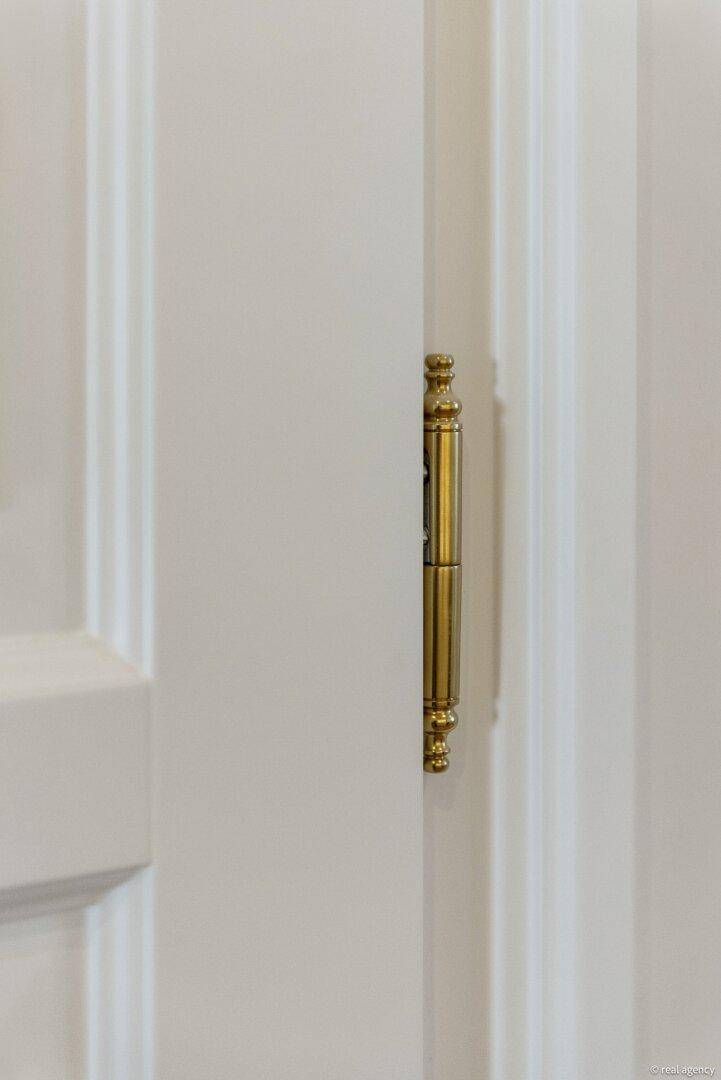 Detail einer verzierten goldenen Türangel an einer weißen Kassettentür.