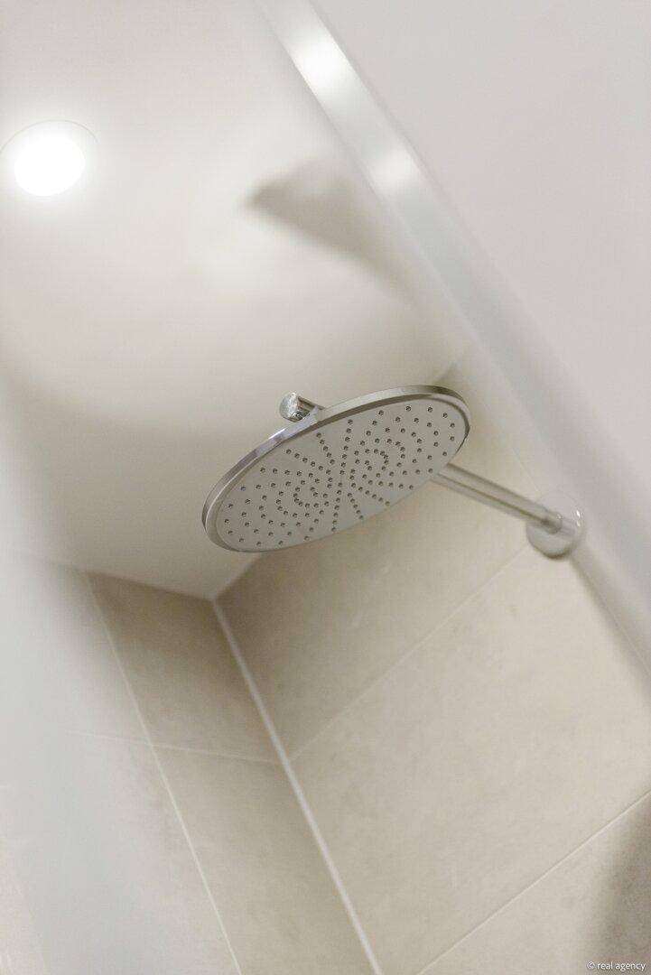 Moderner runder Regenduschkopf an einer hell gefliesten Wand im Badezimmer.