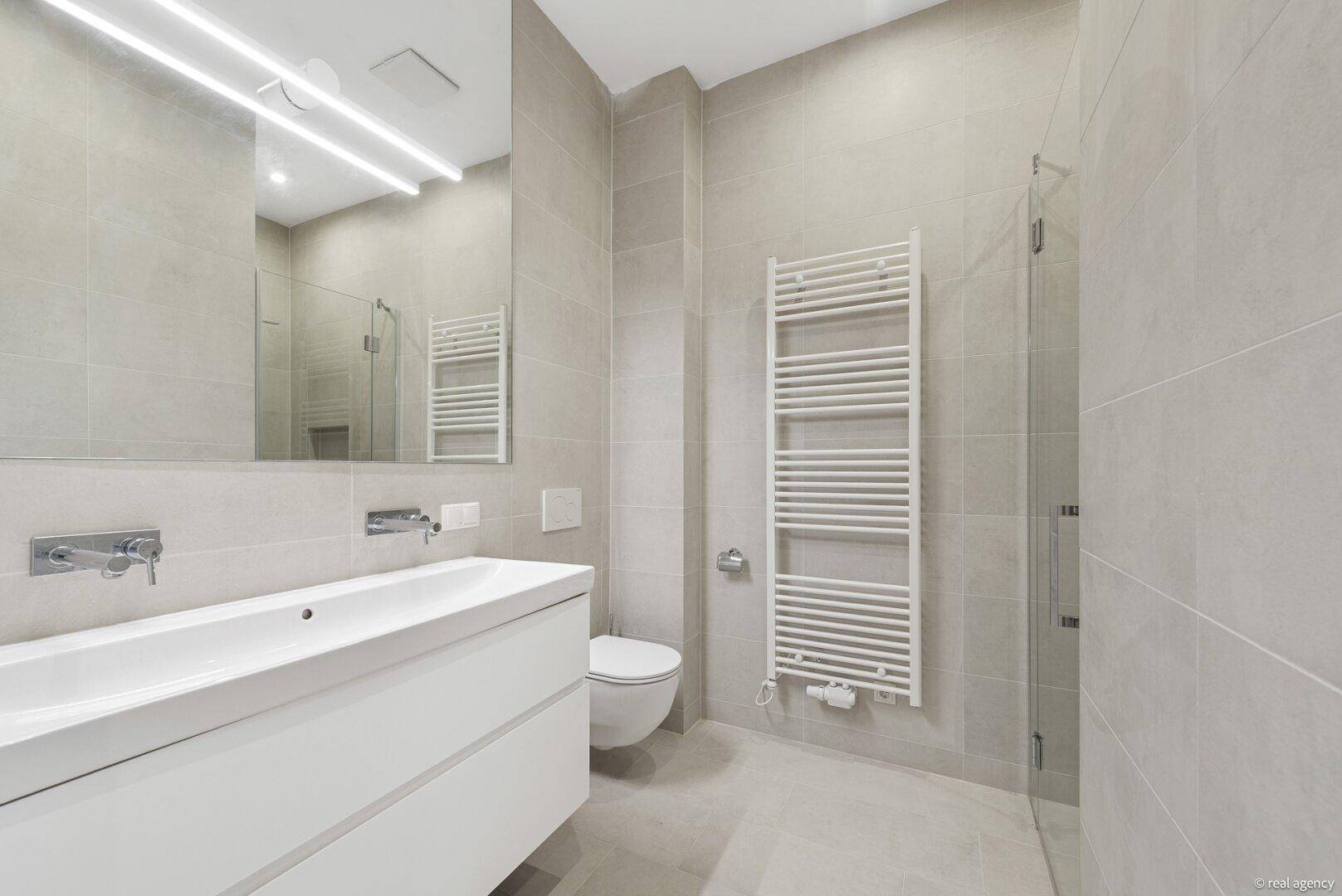 Modernes Badezimmer mit großformatigen Fliesen, schwebendem Waschtisch und begehbarer Dusche.