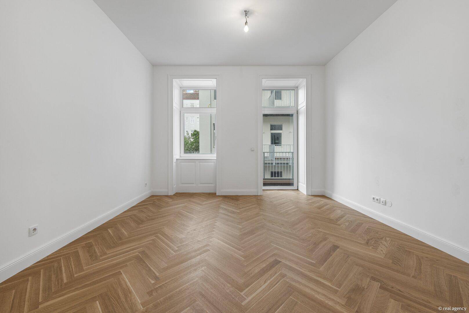 Helles Wohnzimmer mit Fischgrätparkett und Zugang zu einem französischen Balkon.