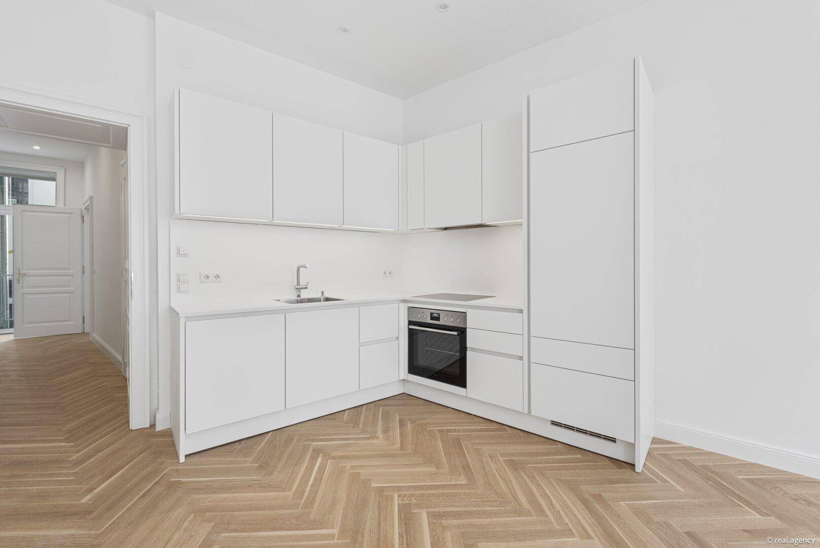 Neue L-förmige Einbauküche in Weiß mit modernen Geräten und elegantem Fischgrätparkett.