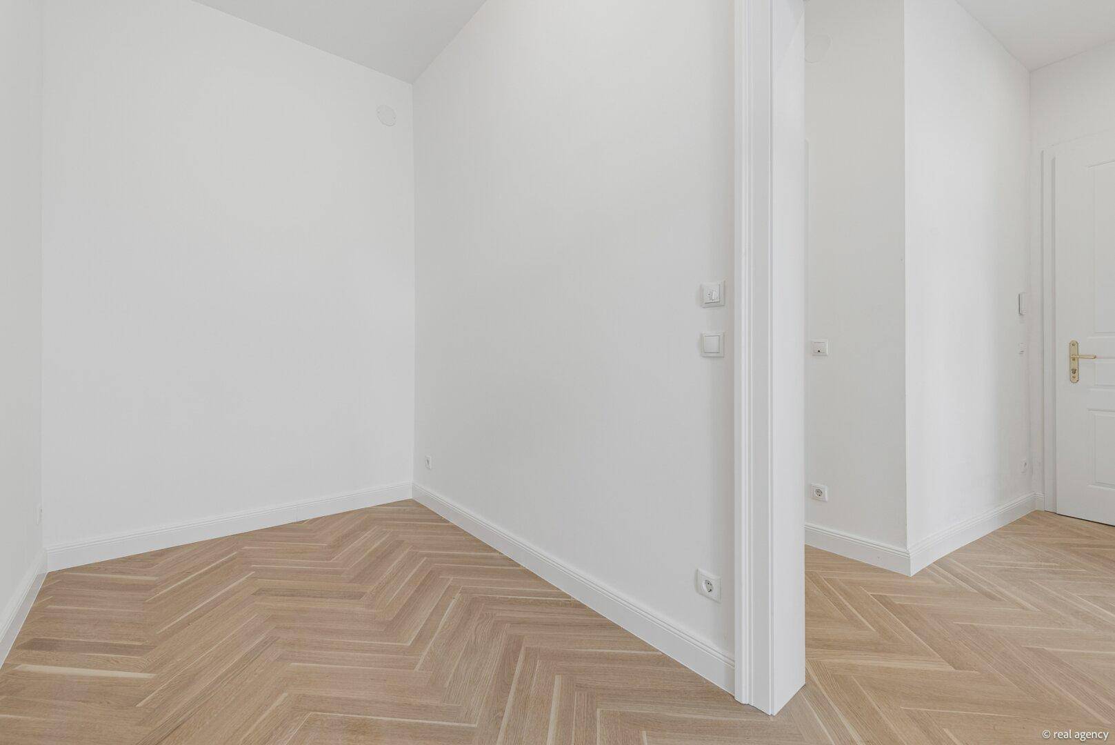 Leerer Raum mit weißen Wänden und elegantem Fischgrätparkett, bereit zur individuellen Gestaltung.