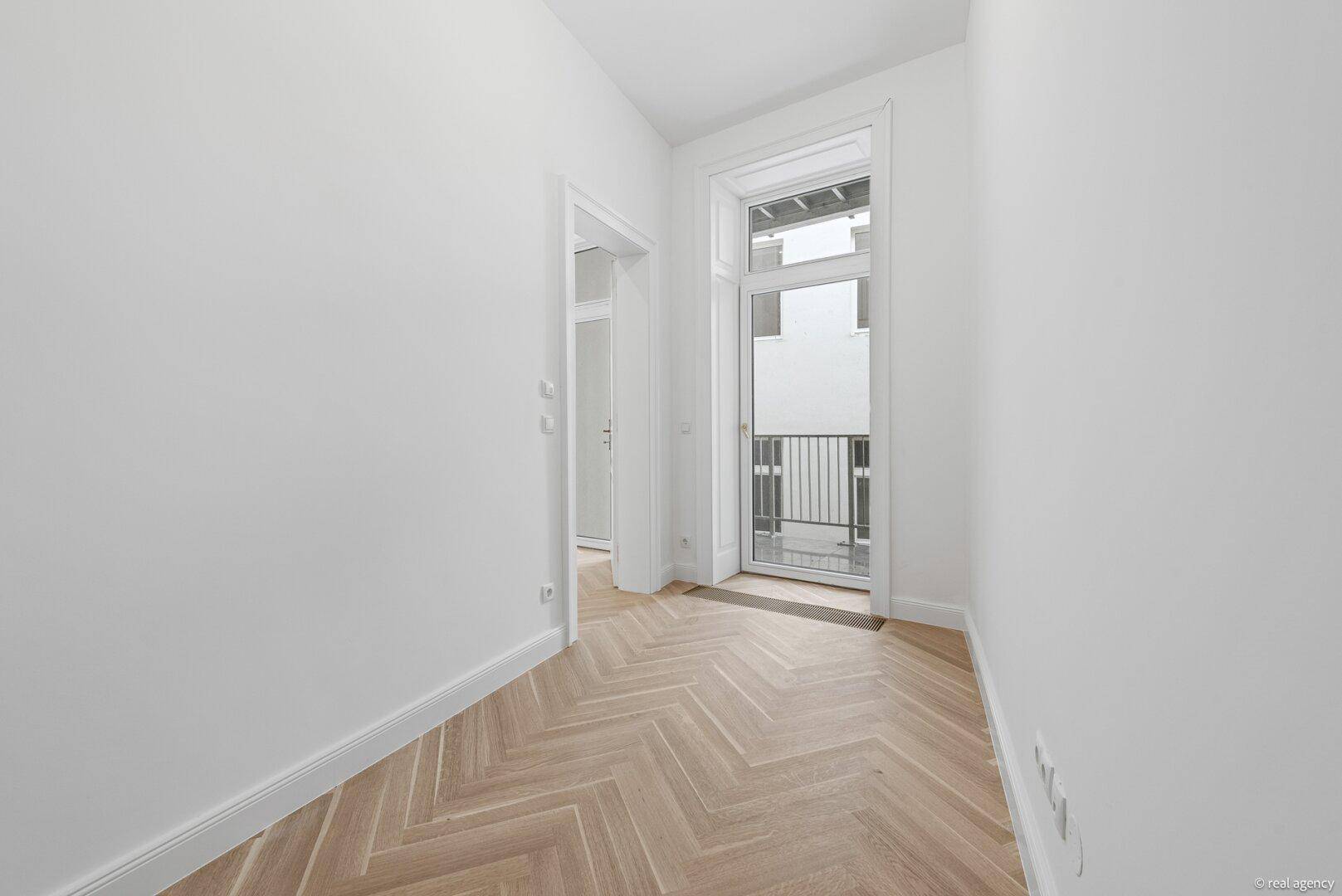 Langer, heller Flur mit Fischgrätparkett und einem französischen Balkon am Ende.