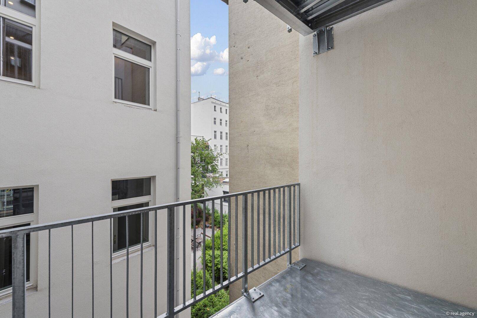 Kleiner Balkon mit Blick auf einen begrünten Innenhof und umliegende Gebäude.