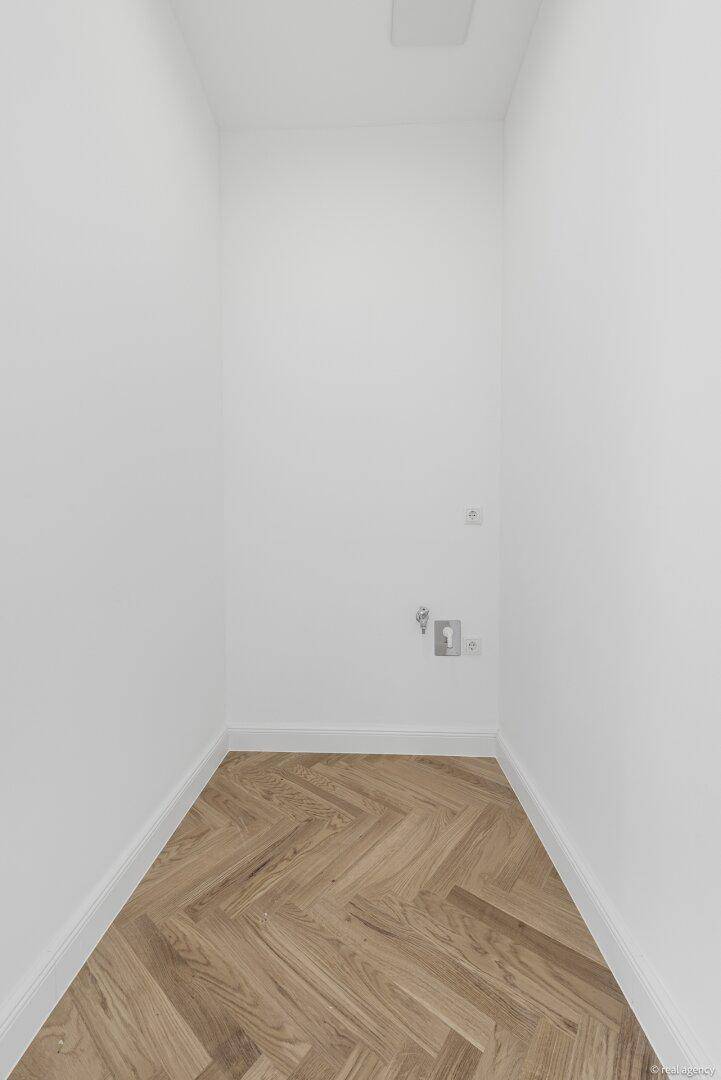 Leerer Hauswirtschaftsraum mit Fischgrätparkettboden und Anschlüssen für Waschmaschine.