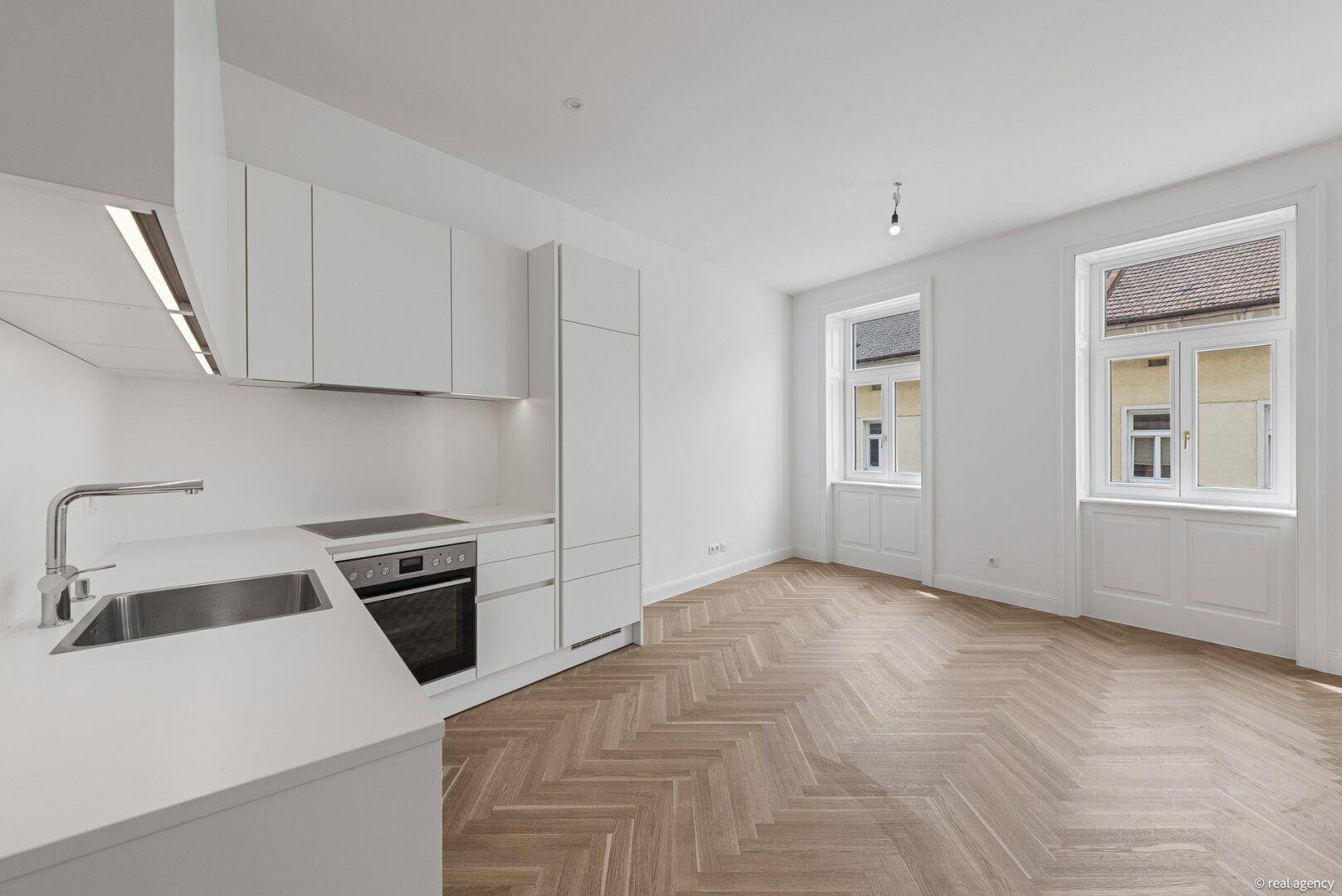 Moderne, helle Einbauküche mit weißen Fronten, integriertem Backofen und Fischgrätparkett.