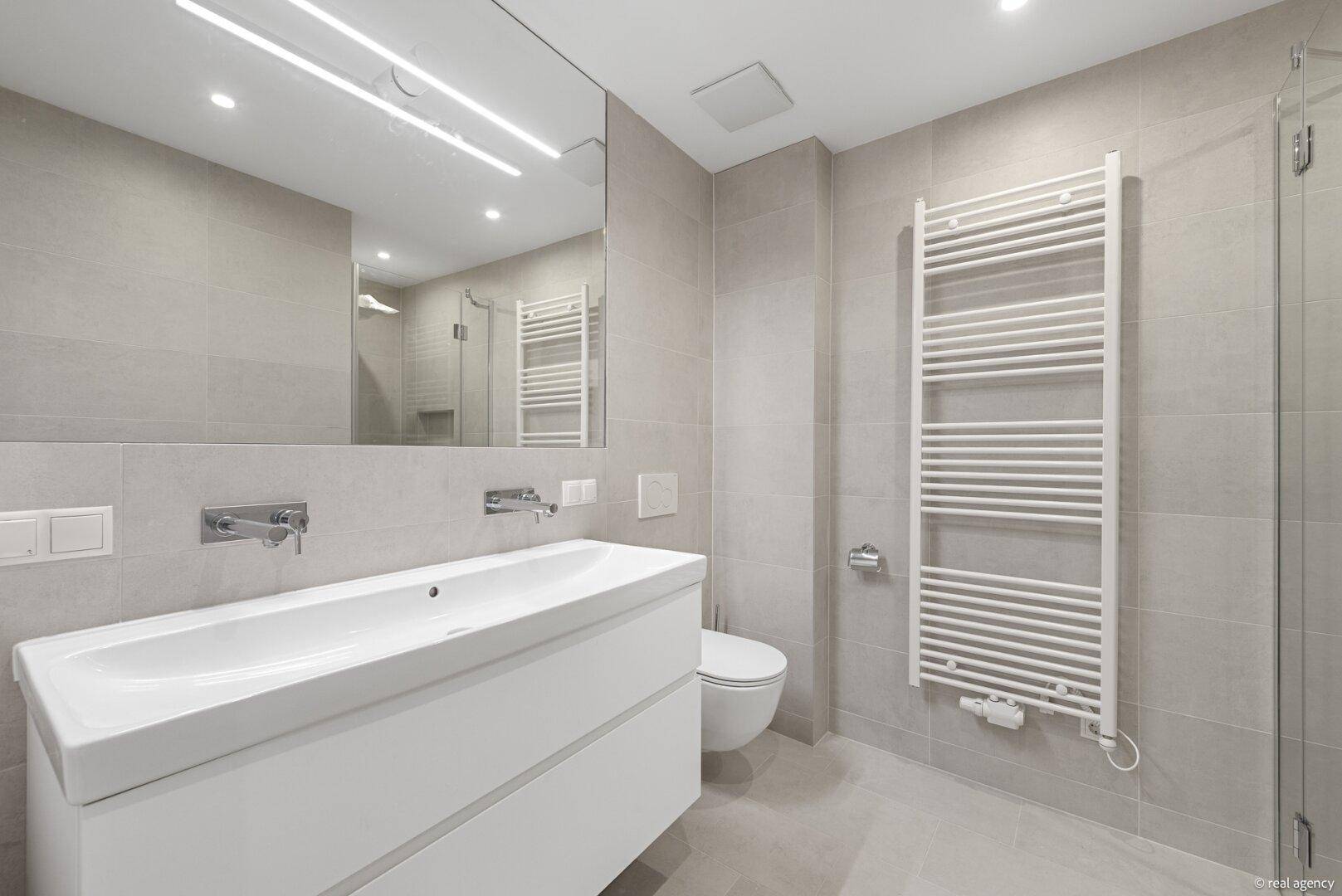Modernes Badezimmer mit großformatigen Fliesen, Einzelwaschbecken und beheiztem Handtuchhalter.