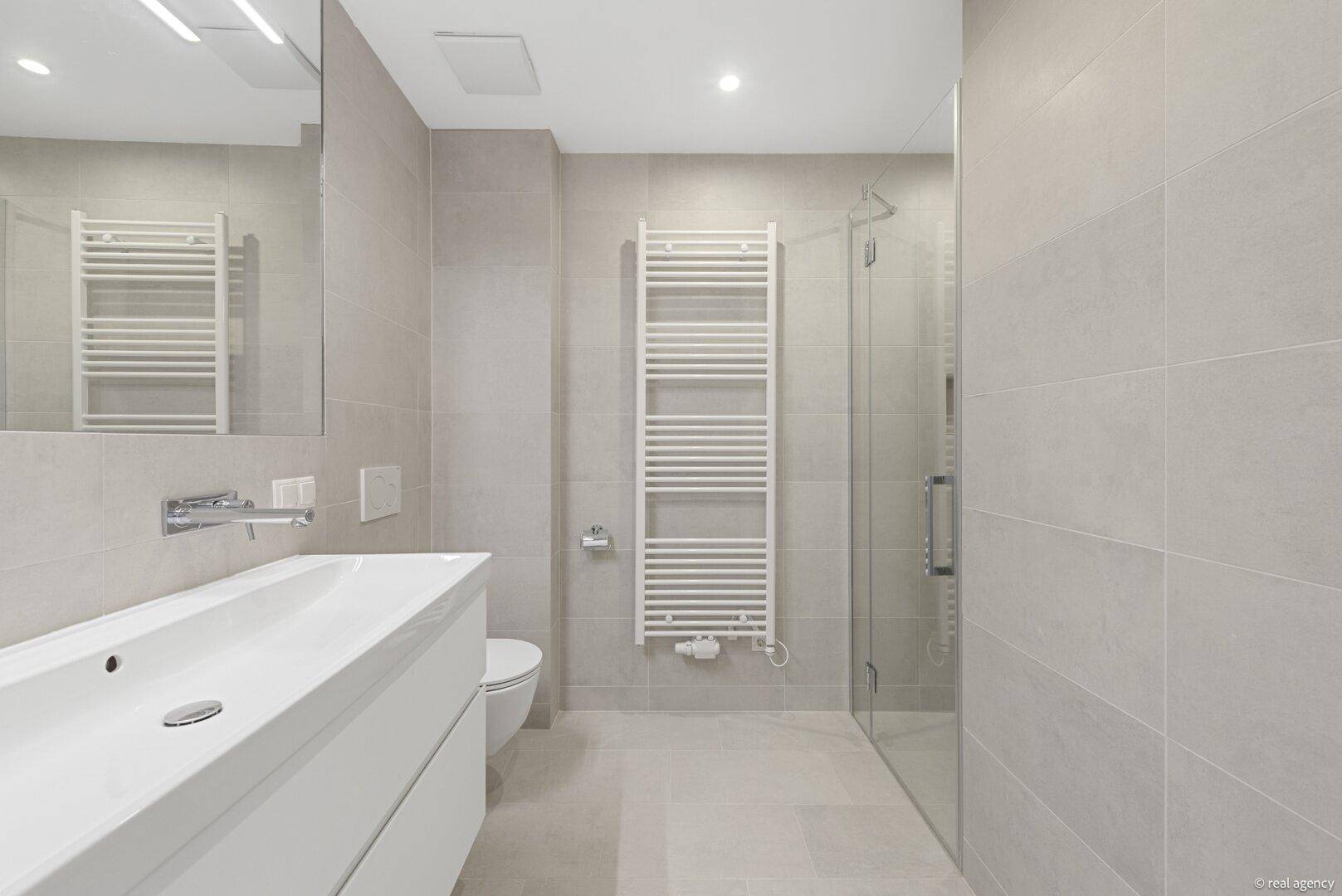 Elegantes Badezimmer mit begehbarer Dusche, modernem Waschtisch und grauen Fliesen.