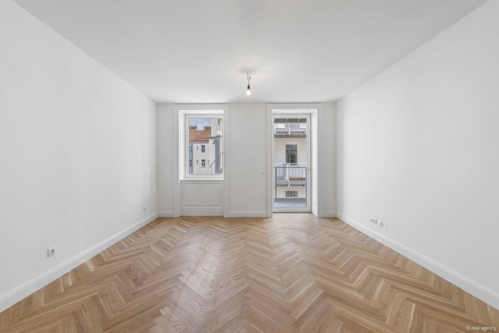 Geräumiges Wohnzimmer mit Fischgrätparkett und Zugang zu einem französischen Balkon.