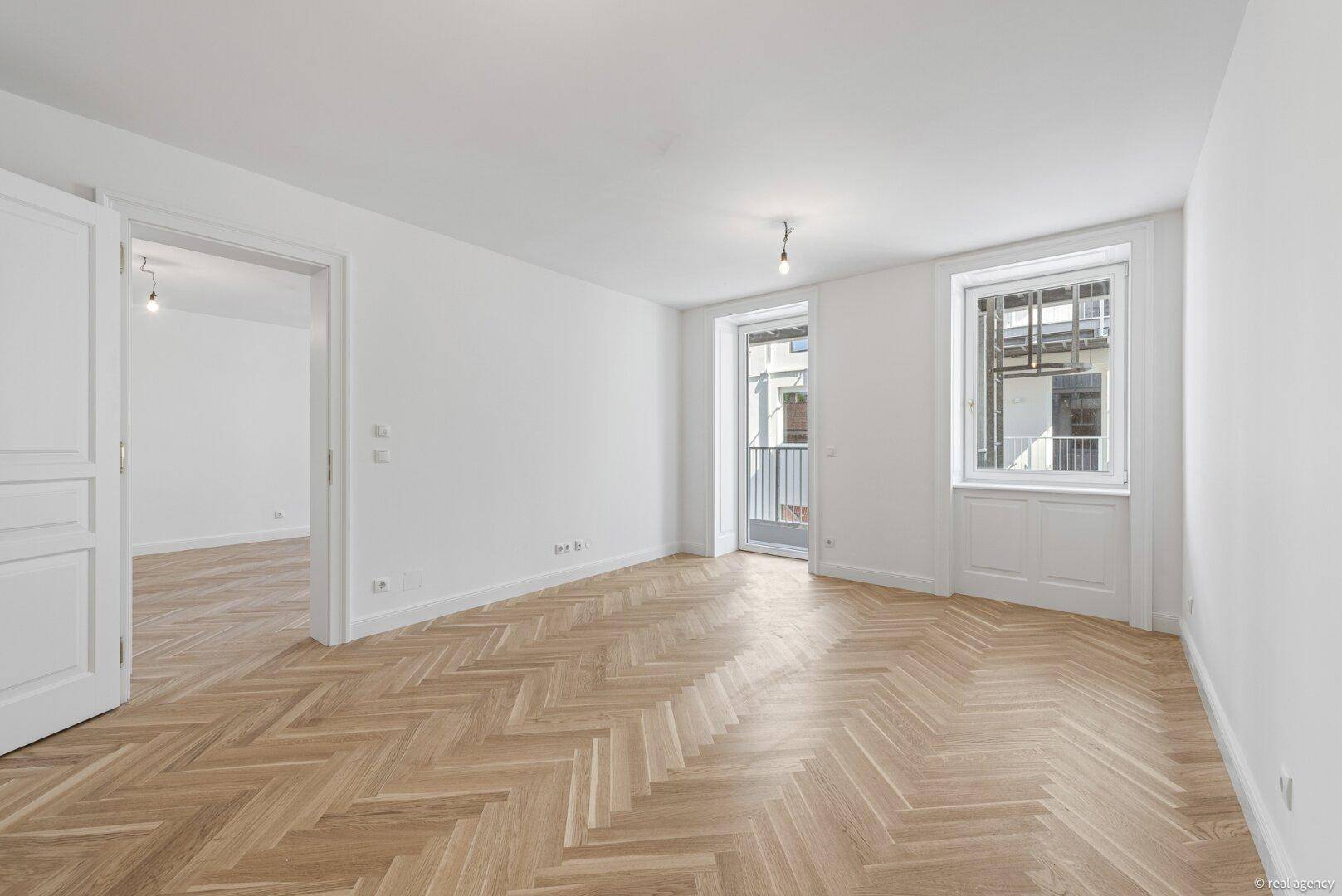 Geräumiges Wohnzimmer mit Fischgrätparkett und Zugang zu einem französischen Balkon.