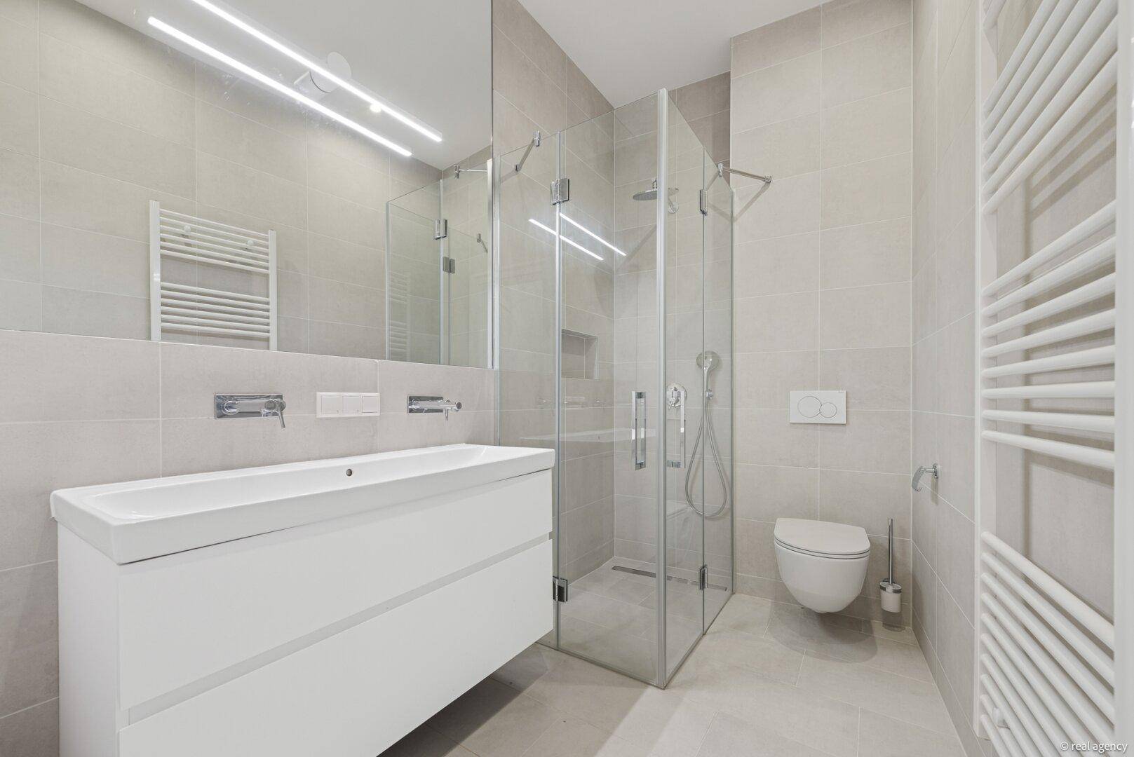 Modernes Badezimmer mit großem Waschtisch, Duschkabine und Wand-WC, alles in hellen Grautönen gehalten.