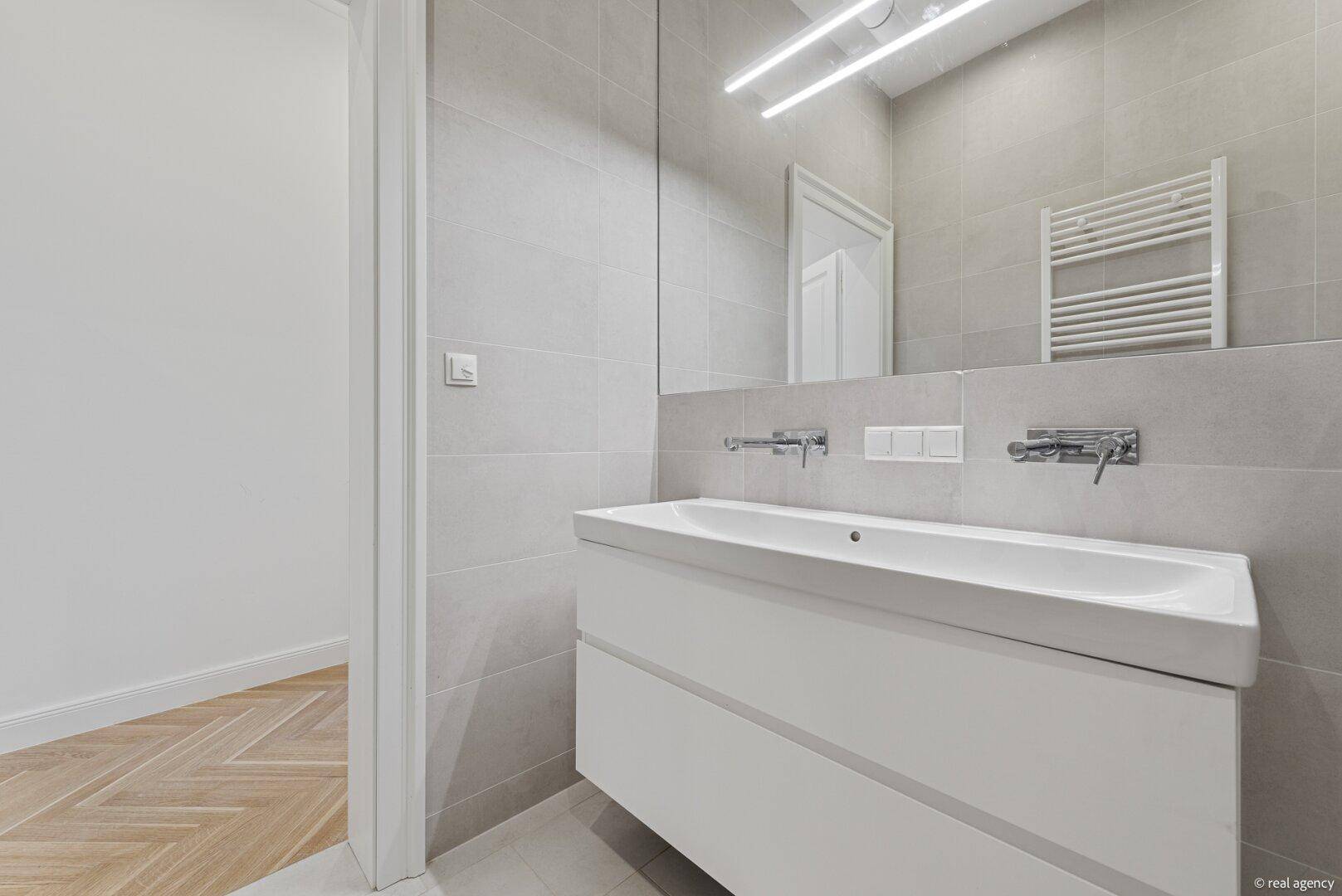 Modernes Badezimmer mit breitem Waschtisch und großem Spiegel, der den Raum optisch vergrößert.