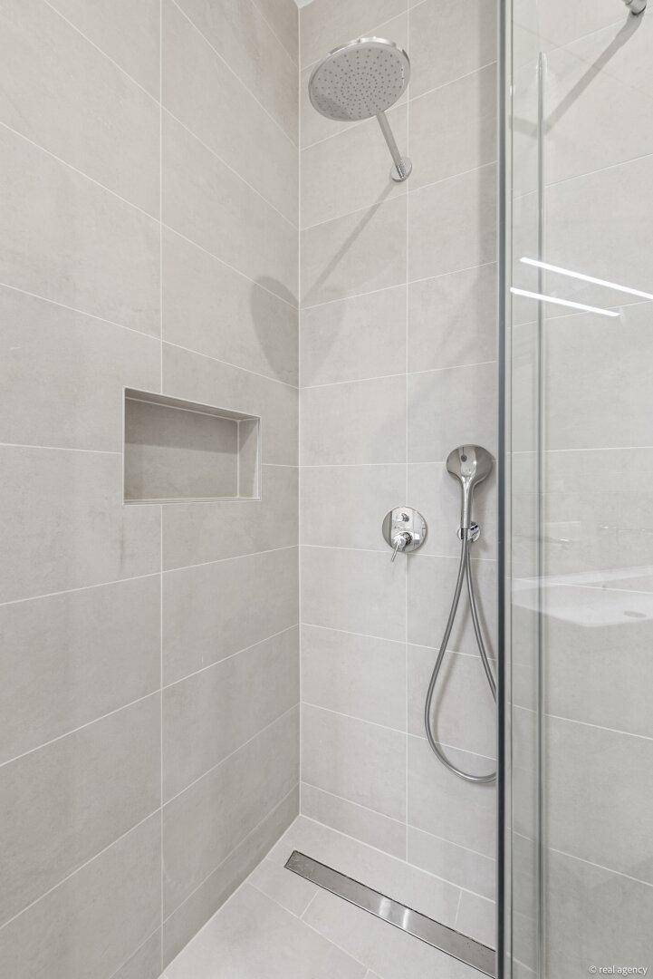 Detaillierte Ansicht einer modernen Duschkabine mit Regendusche und integrierter Nische für Badutensilien.