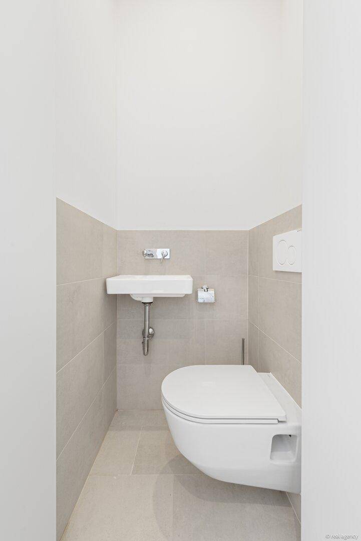 Kleines Gäste-WC mit wandhängender Toilette und kompaktem Waschbecken in hellen Fliesen.