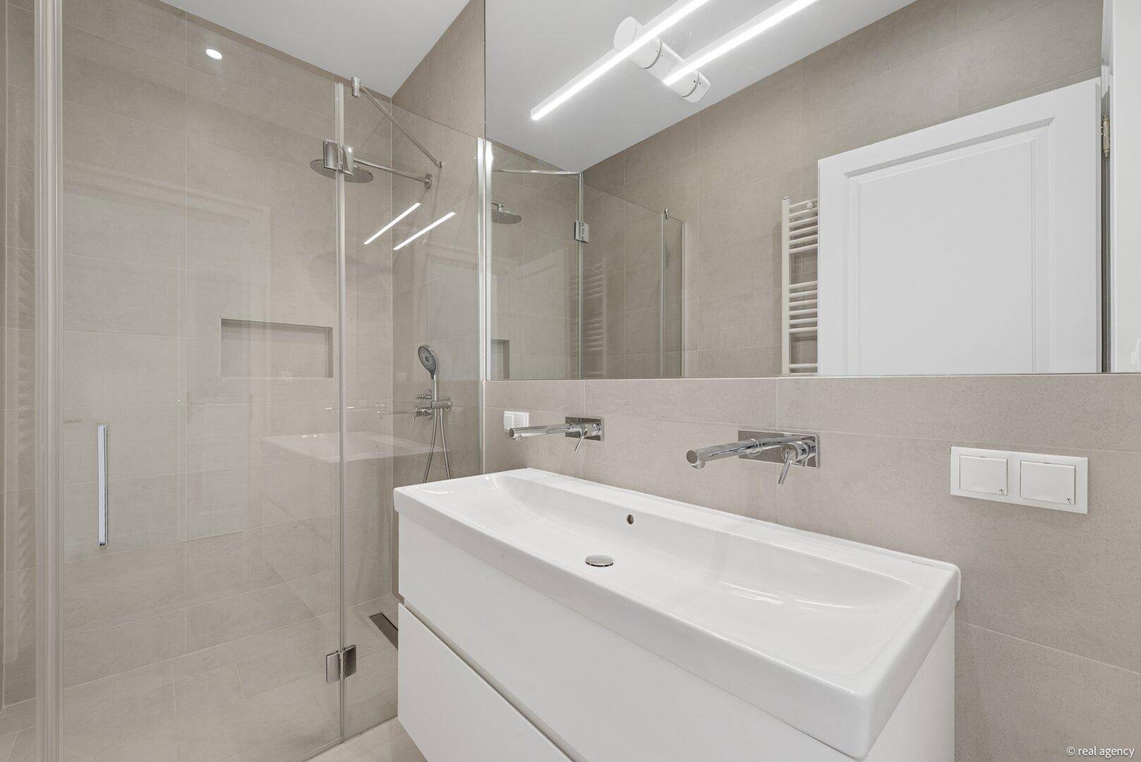 Modernes Badezimmer mit begehbarer Dusche, Einzelwaschbecken und hellen Fliesen in Beige.