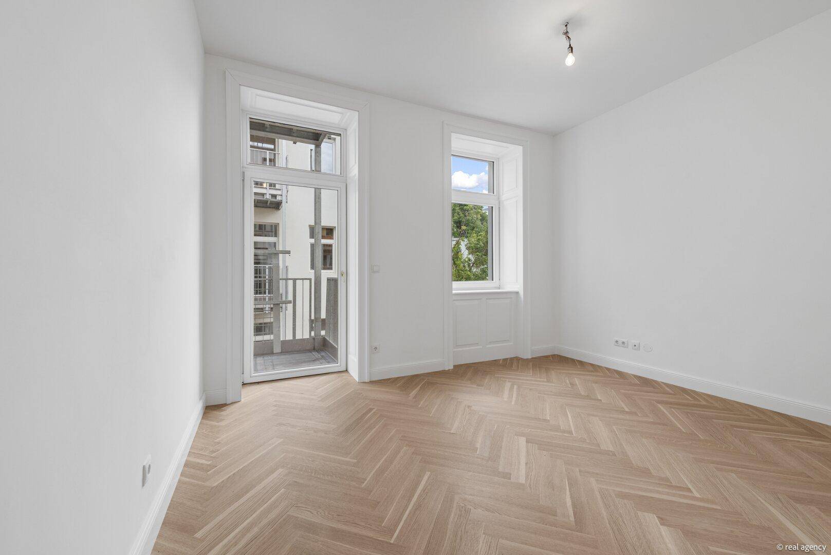 Heller Raum mit Fischgrätparkett und Balkonzugang, ideal für ein Wohn- oder Schlafzimmer.