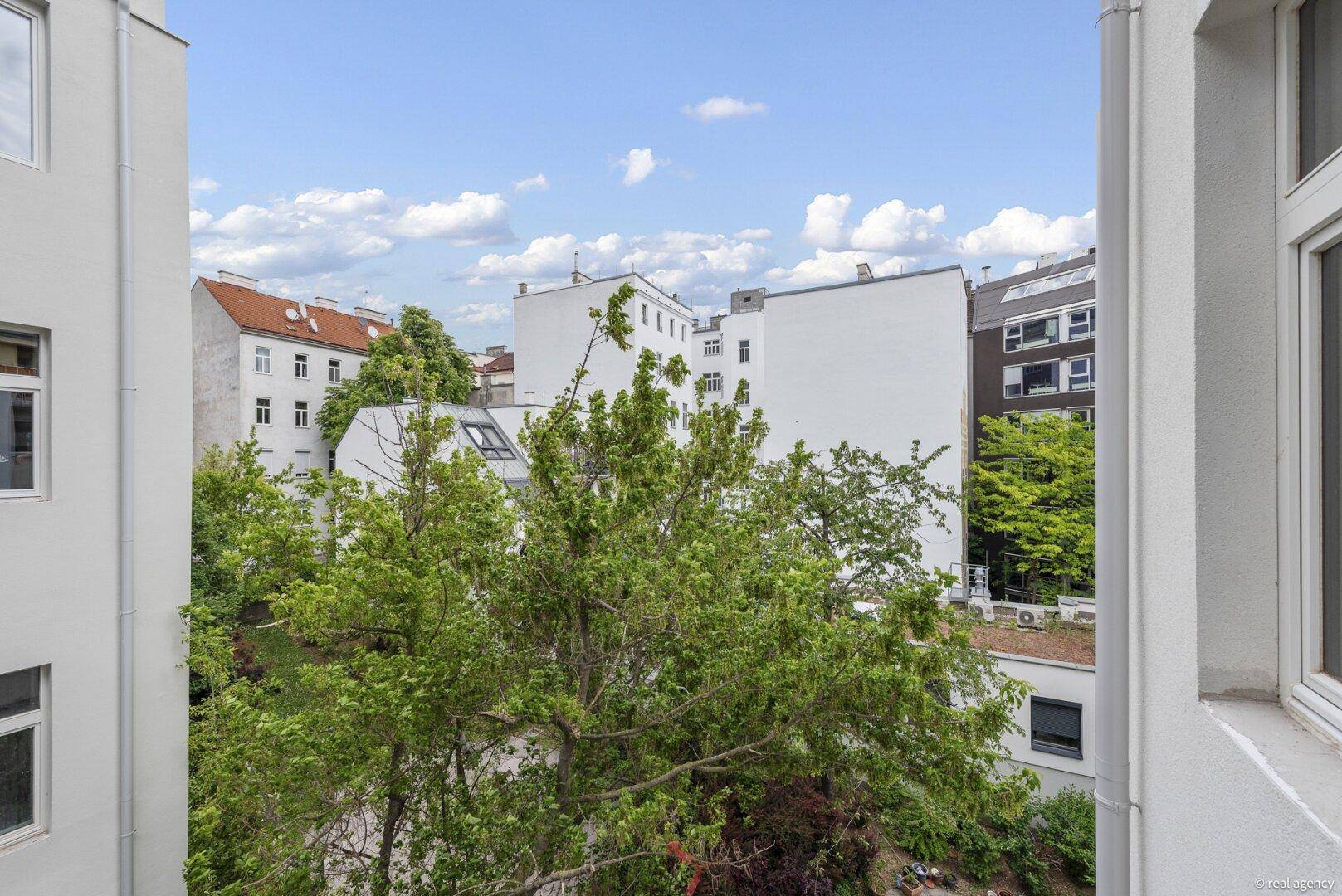 Blick aus dem Fenster auf grüne Bäume und die umliegenden Stadtgebäude.