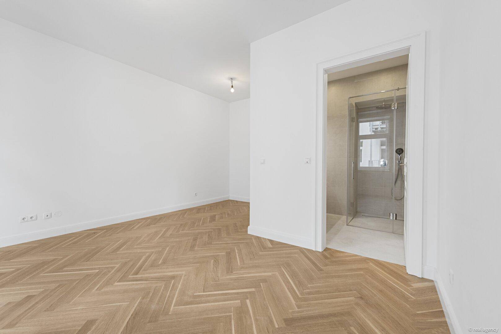 Geräumiges Zimmer mit Fischgrätparkett und Blick auf ein angrenzendes Badezimmer.