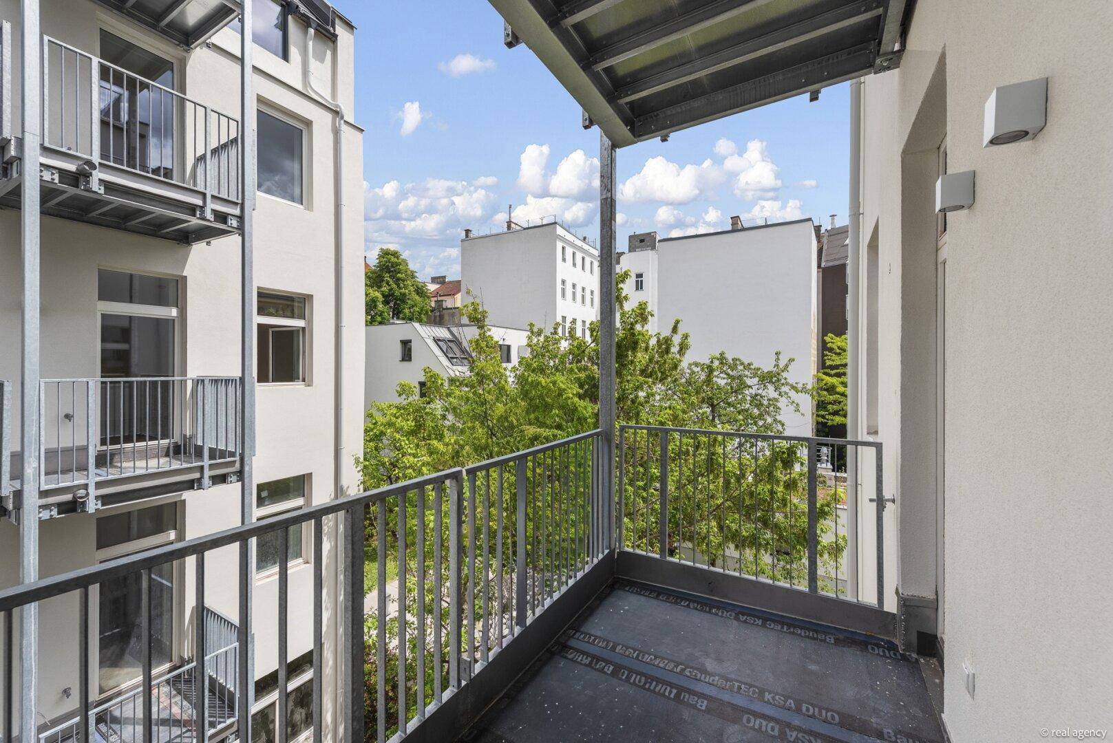 Geräumiger Balkon mit Metallgeländer und Blick auf den grünen Innenhof.
