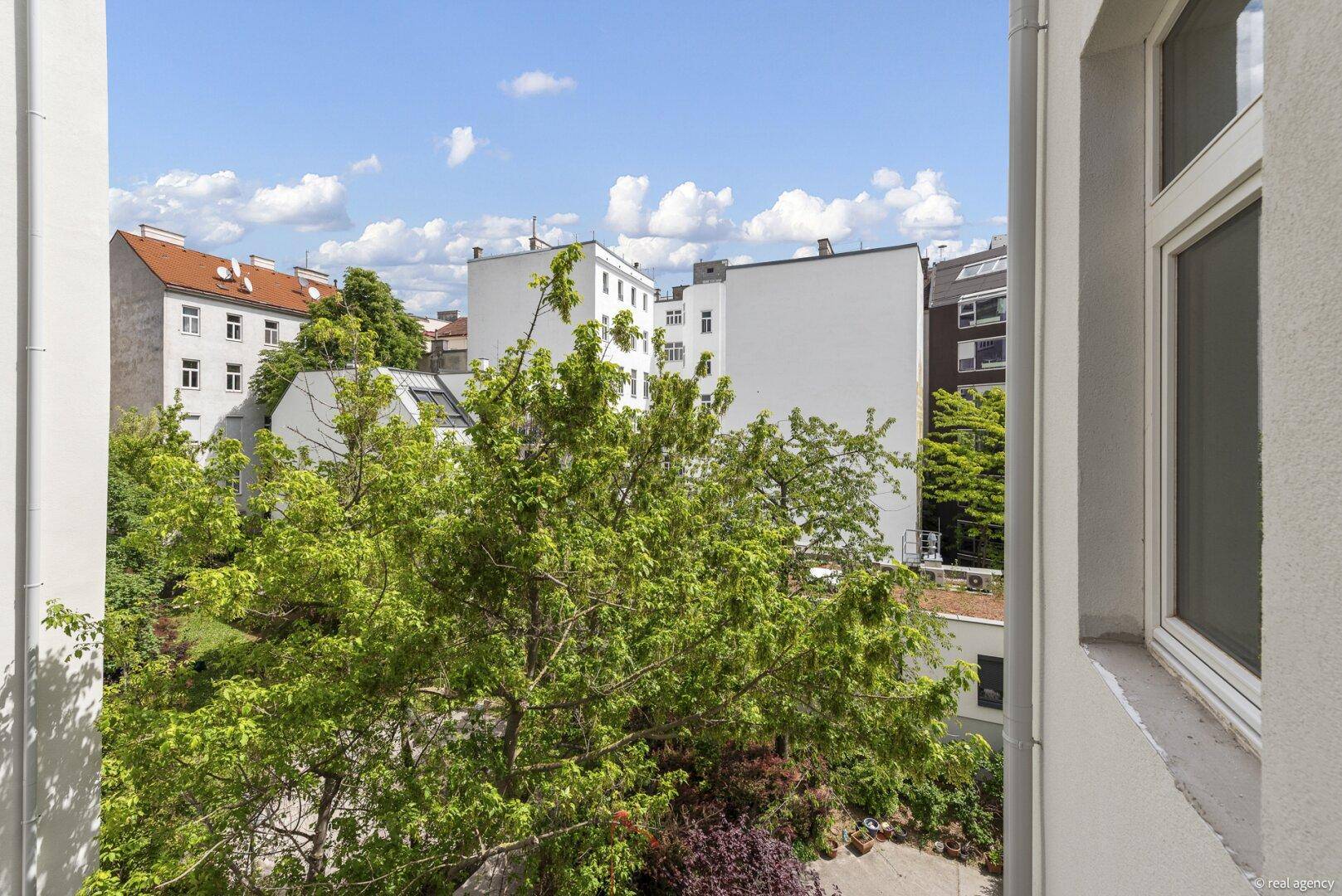 Blick aus dem Fenster auf den grünen Innenhof und die umliegenden Gebäude.