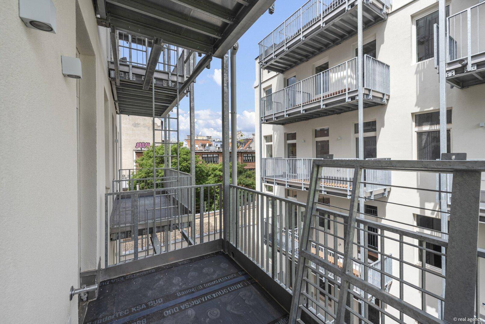 Balkon mit Metallgeländer und Blick auf die umliegenden Gebäude und den Innenhof.