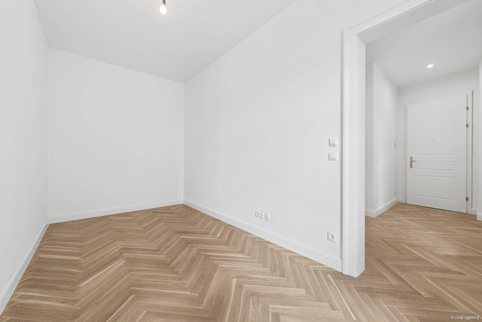 Ruhiges Schlafzimmer mit hellem Fischgrätparkett und weißen Wänden, bereit zur individuellen Gestaltung.
