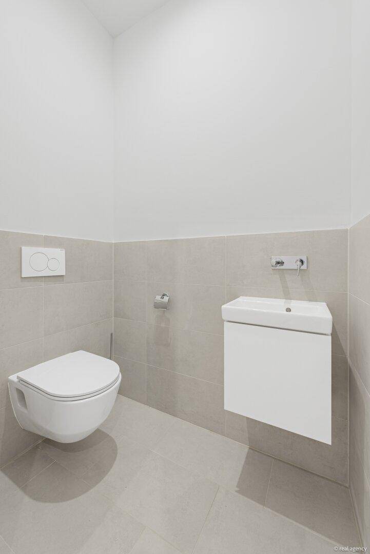Modernes Gäste-WC mit wandhängender Toilette und kleinem Waschtisch in neutralen Farbtönen.