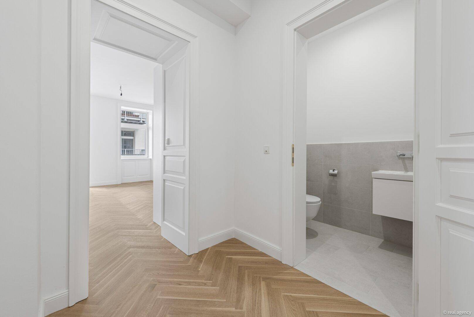 Heller Flur mit Fischgrätparkett und Zugang zu einem Zimmer sowie dem modernen Gäste-WC.