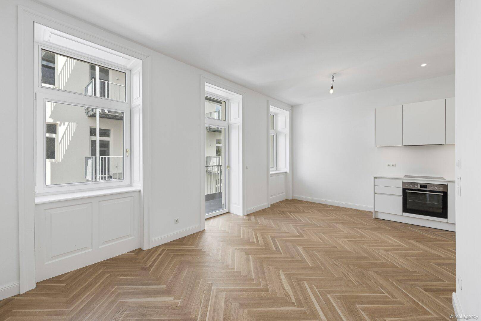Heller Wohnbereich mit Fischgrätparkett, moderner Küche und Zugang zu einem Balkon.