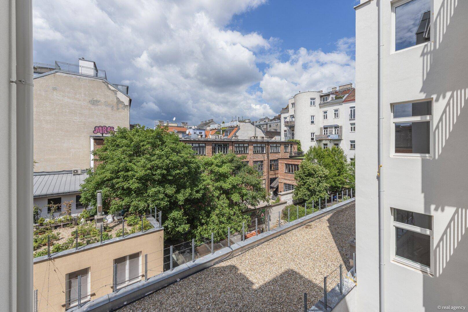 Blick aus dem Fenster auf die umliegenden Dächer, Bäume und städtische Gebäude.