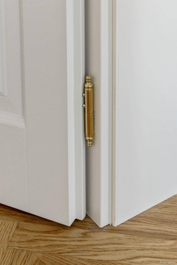 Detailansicht eines goldenen Türscharniers an einer weißen Tür.