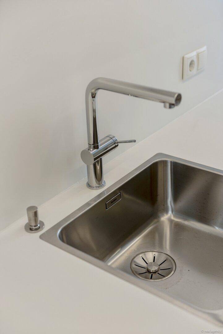 Edelstahlspüle mit modernem Wasserhahn und weißer Arbeitsplatte in der Küche.