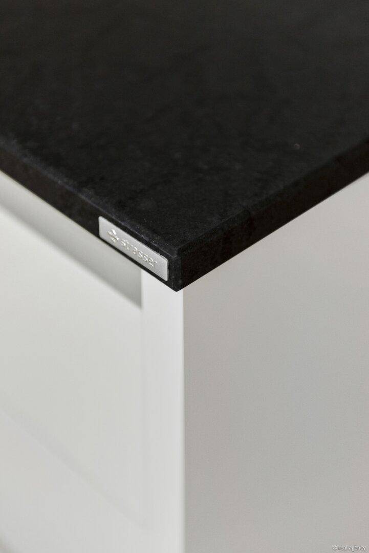 Detailansicht einer dunklen Granitarbeitsplatte mit Schüller-Markenplakette in einer modernen Küche.