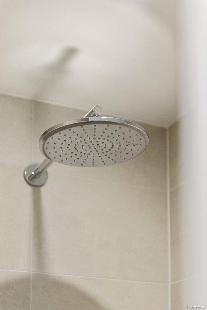 Moderne Regendusche mit großem Duschkopf und hellen Fliesen im Badezimmer.