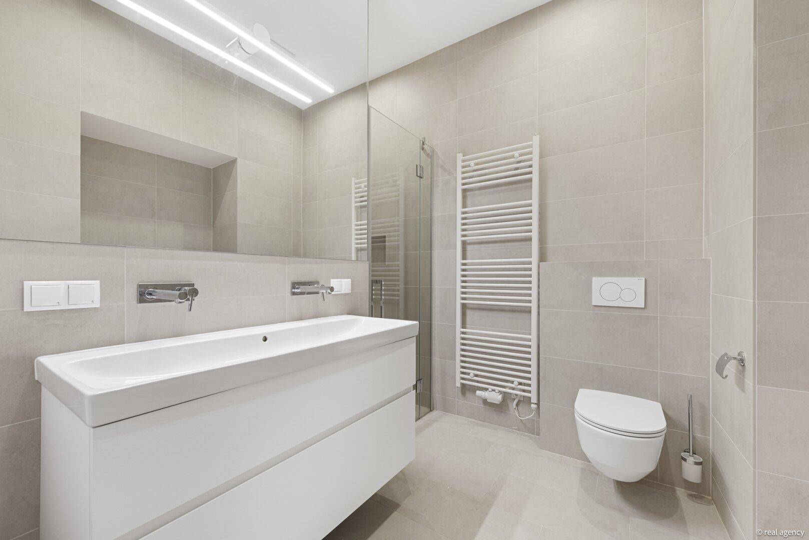 Modernes Badezimmer mit großen Fliesen, wandhängendem WC und beheiztem Handtuchhalter.