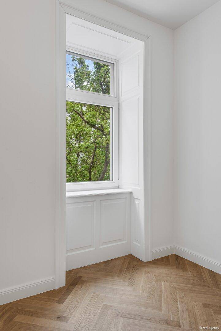 Detailansicht eines hohen Fensters mit Holzeinfassung und Blick ins Grüne.