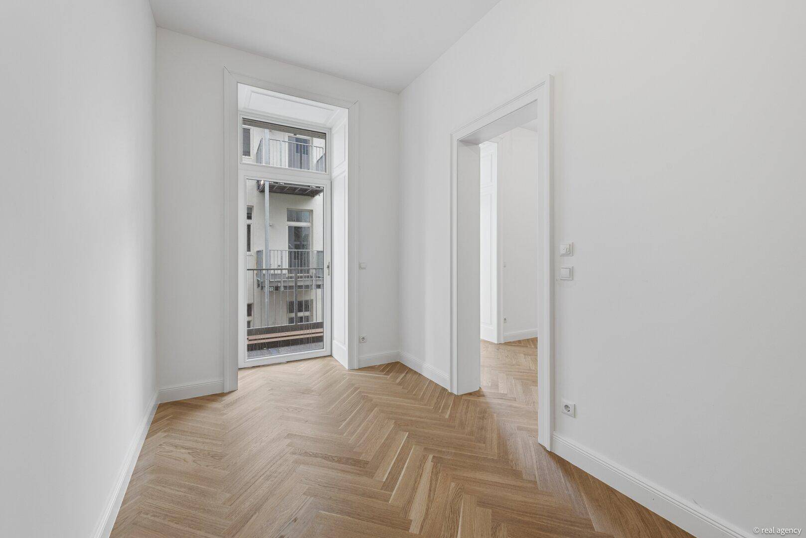 Helles Zimmer mit Fischgrätparkett und Zugang zu einem französischen Balkon.