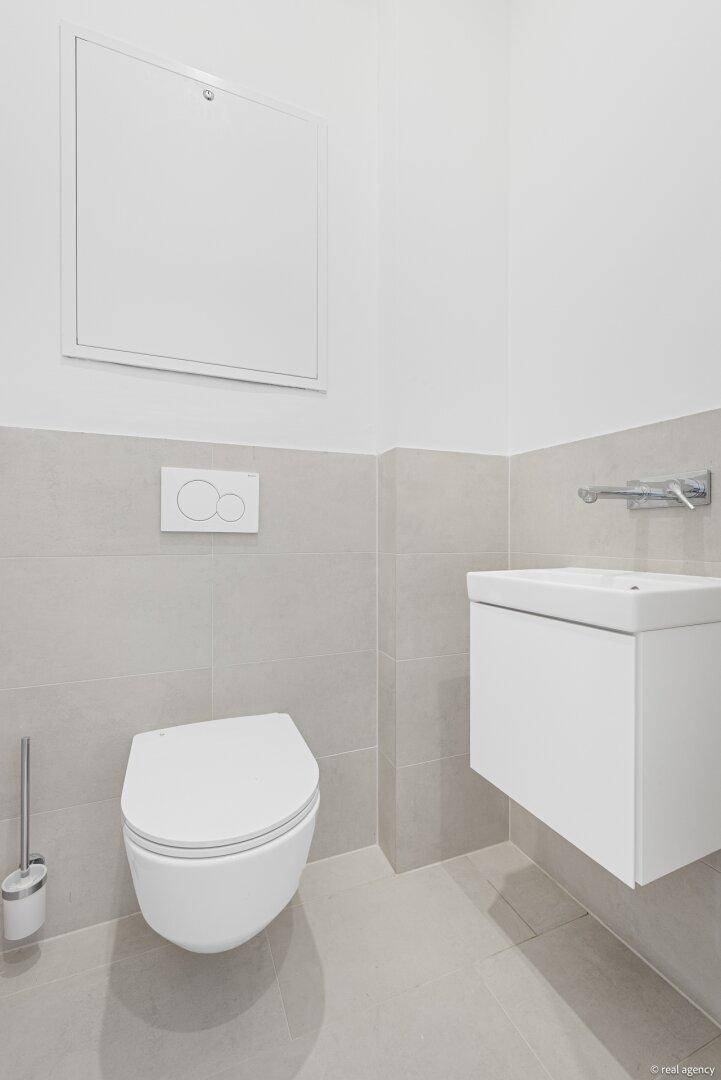 Modernes Gäste-WC mit wandhängender Toilette und kleinem Waschbecken, in hellgrauen Fliesen.