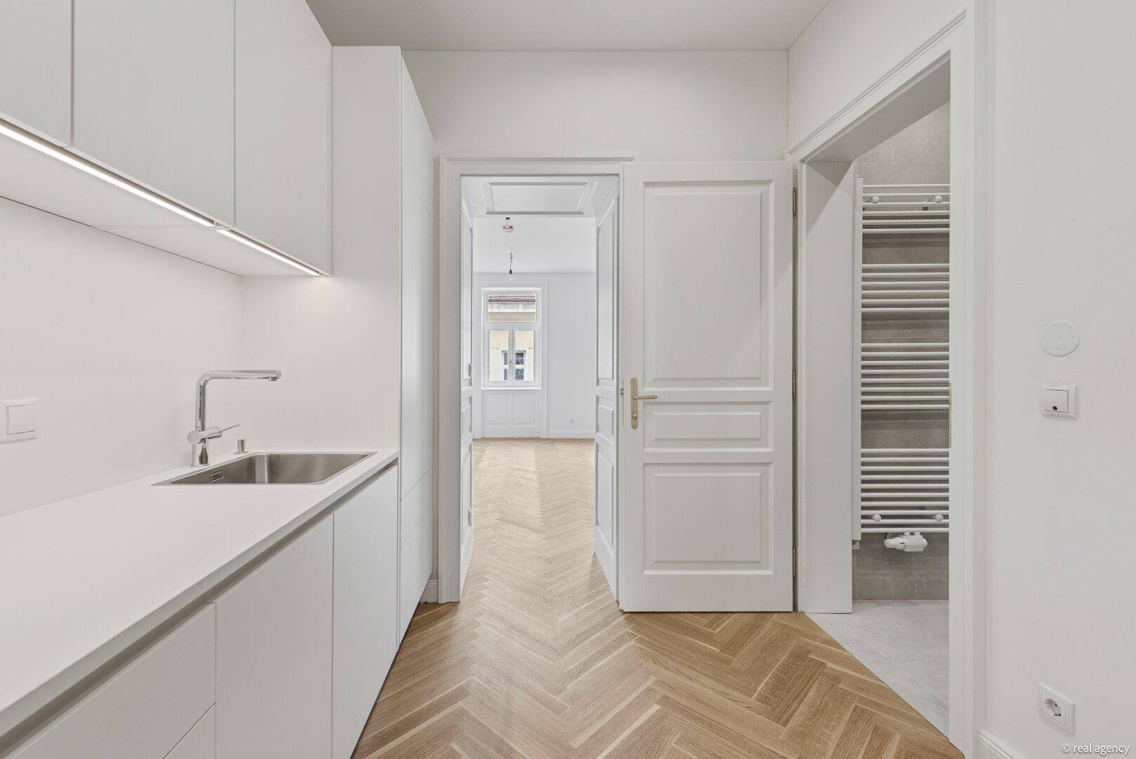 Helle Küche mit Fischgrätparkett, die zu einem Wohnraum und einem modernen Badezimmer führt.