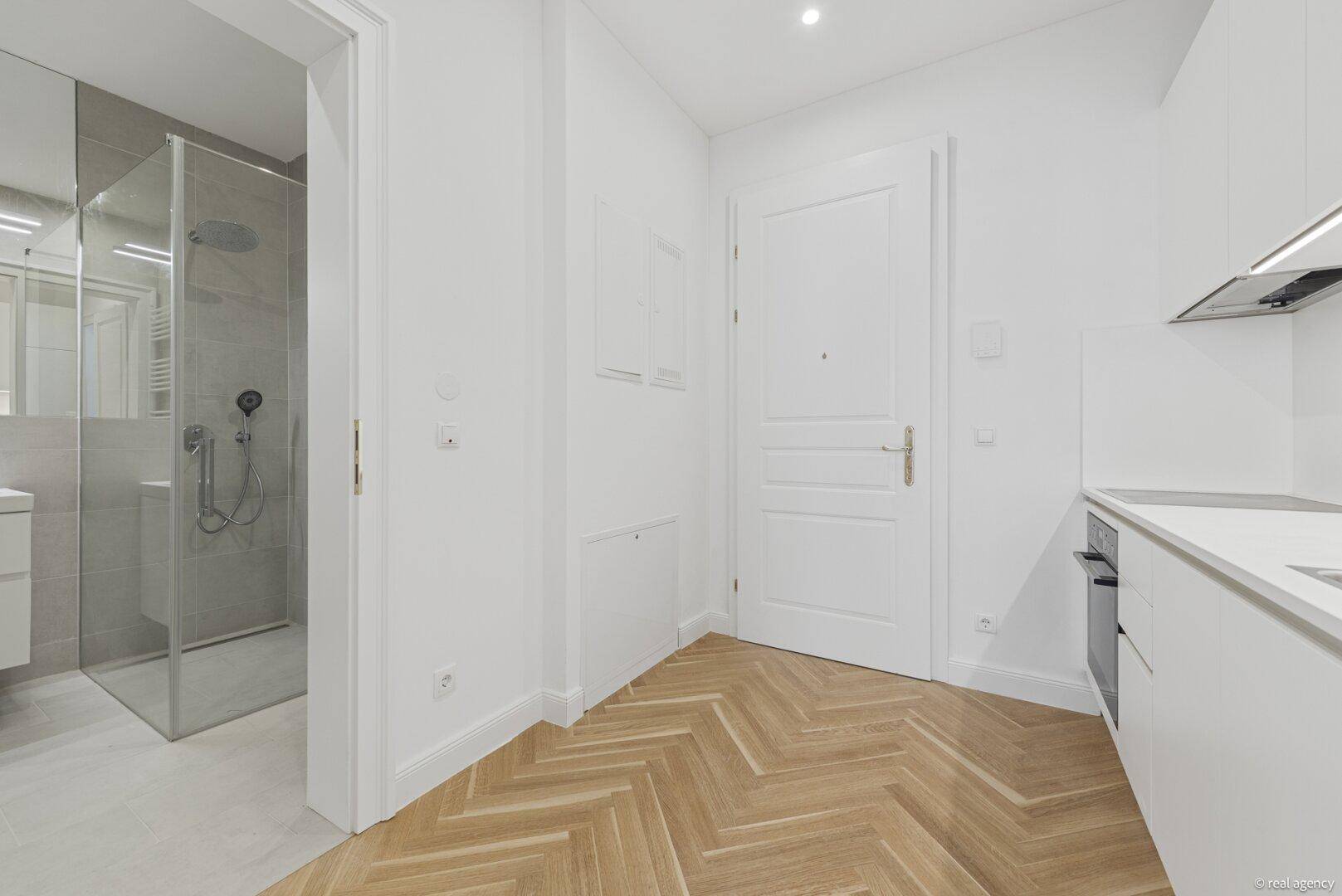 Heller Flur mit Fischgrätparkett, der zu einem modernen Badezimmer und einer Küchenzeile führt.