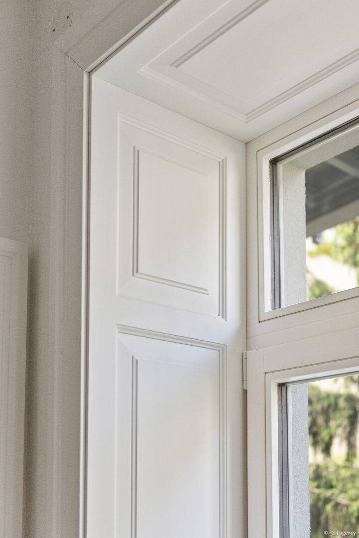 Detailansicht eines weißen Fensterrahmens mit dekorativen Paneelen, die den klassischen Stil unterstreichen.