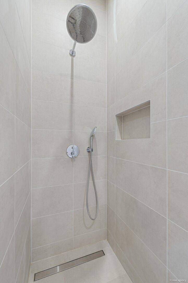 Detailaufnahme einer modernen Dusche mit Regenduschkopf und Handbrause in einem hell gefliesten Bad.