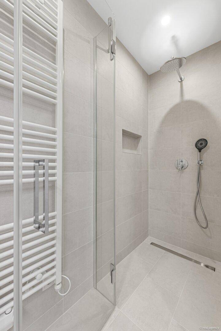 Modernes Badezimmer mit begehbarer Dusche, Regenduschkopf und beheiztem Handtuchhalter in hellen Grautönen.