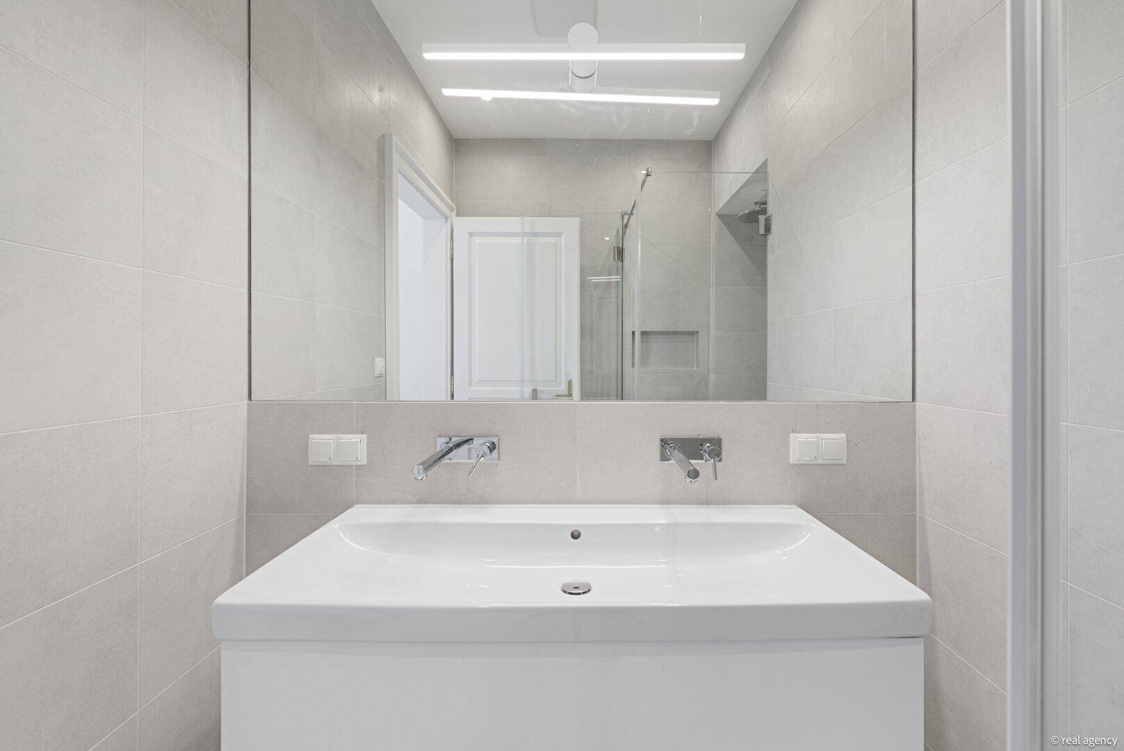 Modernes Badezimmer mit großem Spiegel, integrierter Beleuchtung und minimalistischem Waschbecken.