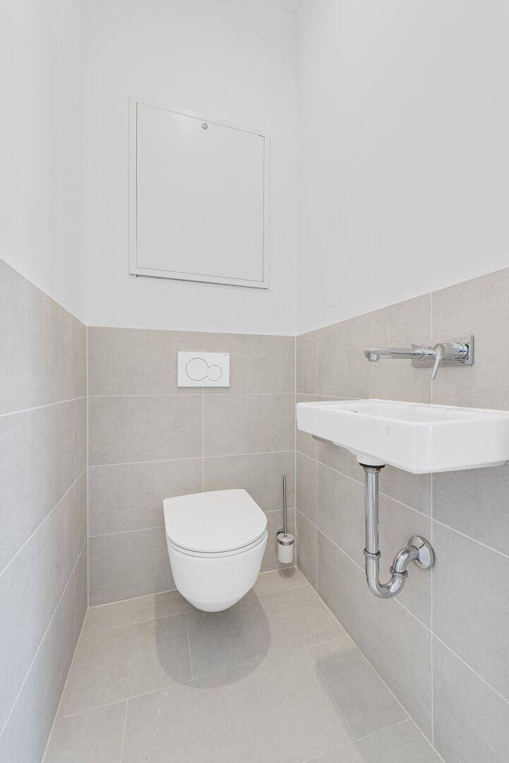 Helles Gäste-WC mit wandhängender Toilette, kleinem Waschbecken und Fliesenboden.