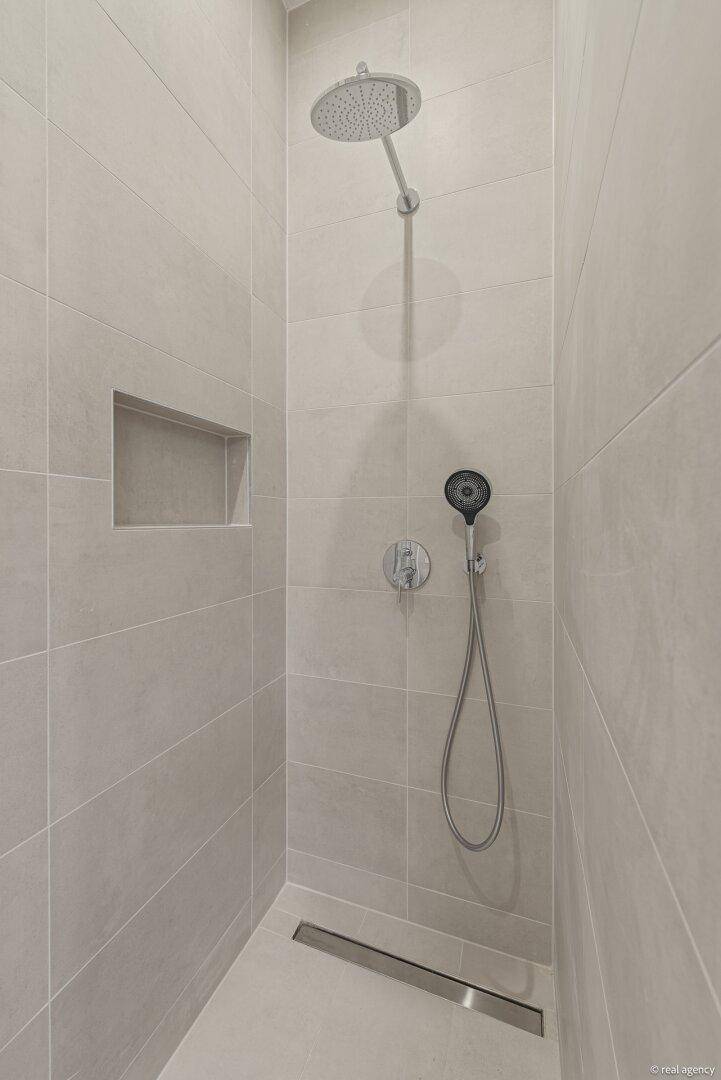 Moderne begehbare Dusche mit Regenduschkopf, Handbrause und integrierter Ablage.