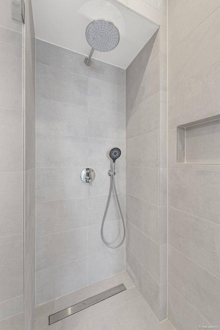 Moderne Duschkabine mit Regendusche und Handbrause, ausgestattet mit hellgrauen Fliesen.