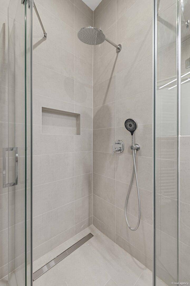 Geräumige, begehbare Dusche mit Regenduschkopf und integrierter Nische in hellen Fliesen.
